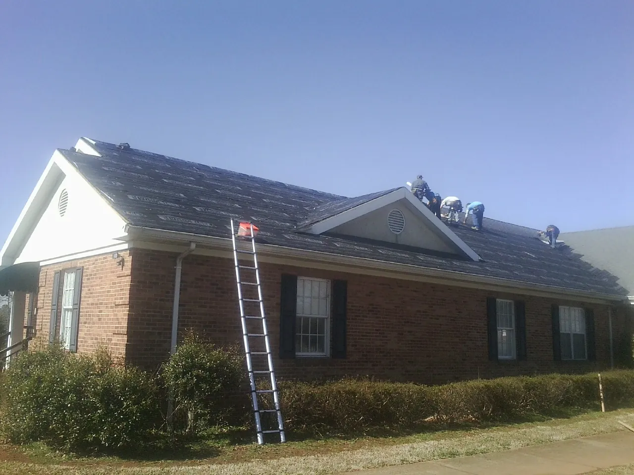 Crew tearing shingles off a brick ranch roof with a ladder set — Emergency Roof Repair work by our crew in Middlesex