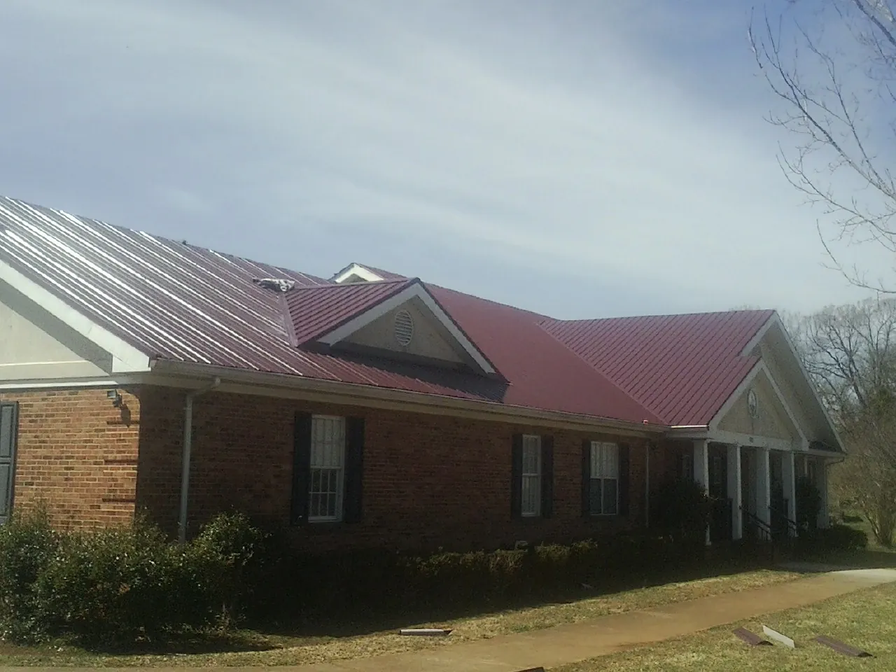 Red metal roof with gabled entries on a long brick building, from a Hail Damage Roof Repair job in Middlesex